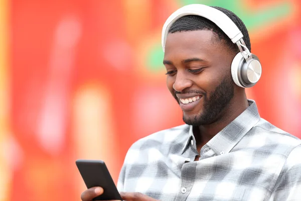 Happy black man listens to the music with headphones and phone on red background