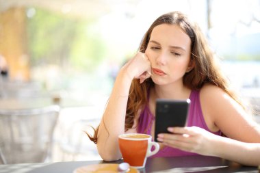 Sinirli bir kadın restoranın terasında akıllı telefonu kontrol ediyor.