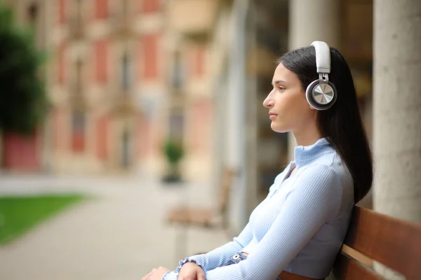 Side view portrait of a serious woman sitting in a bench listening to music