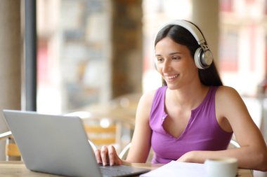 Kahve dükkanının terasında dizüstü bilgisayar ve kulaklıkla mutlu öğrenci e-öğrenimi.