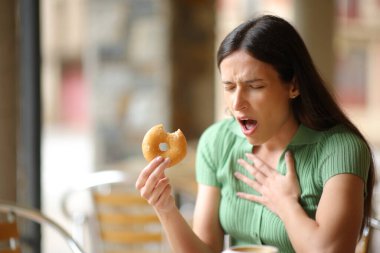 Stressed woman choking eating doughnut in a bar terrace clipart