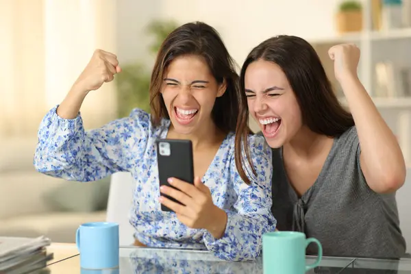 Excited women checking phone celebrating success at home