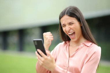 Sokakta yürüyen heyecanlı kadın telefonu kontrol ediyor ve başarıyı kutluyor.