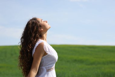 Yeşil alanda temiz hava soluyan beyaz elbiseli bir kadının profili.