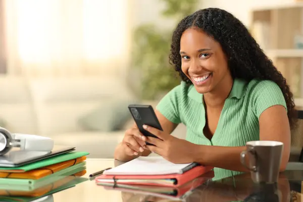 Stock image Happy black student using phone looking at you at home