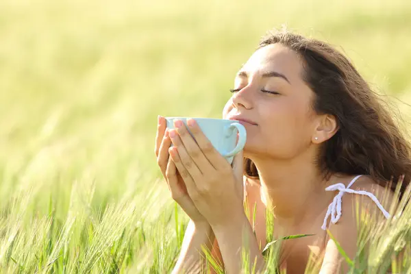 Relaxed woman smelling coffee in nature at sunset