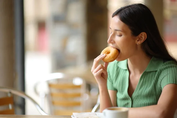 Woman in a restaurant terrace eating doughnut for breakfast