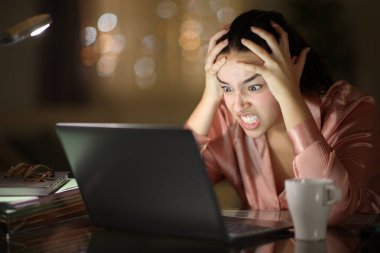 Sinirli tele-sekreter gece merkez büroda dizüstü bilgisayarla çalışıyor.