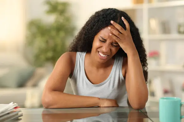Black woman suffering head ache sitting at home