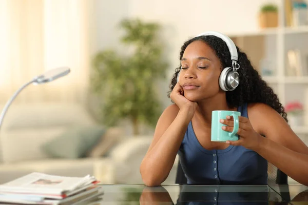 Black woman wearing headphone relaxing listening music drinking coffee at home