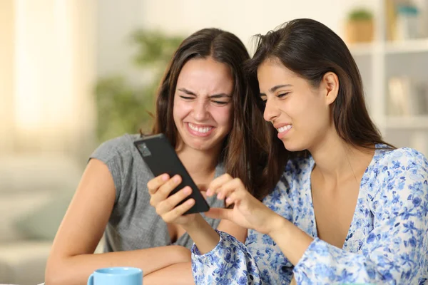 Disgusted women checking nasty cell phone content at home