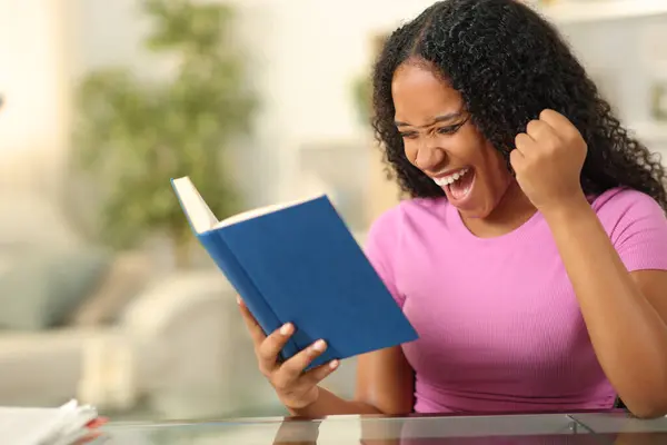 黑人兴奋地阅读一本在家里庆祝的纸质书 图库照片