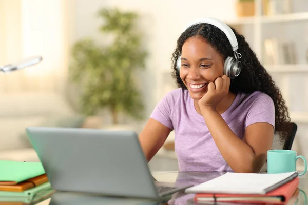 Happy black student eleaning online with laptop and headphone at home