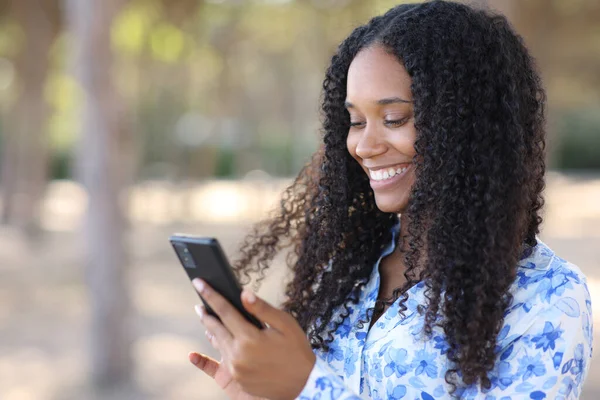 Szczęśliwa Czarna Kobieta Pomocą Telefonu Komórkowego Uśmiecha Się Spaceruje Parku Obrazy Stockowe bez tantiem