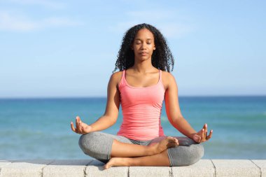 Sahilde yoga yapan siyahi bir kadının portresi.