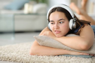 Evde bir halıya uzanmış kulaklıkla müzik dinleyen hayal kırıklığına uğramış bir kadın.