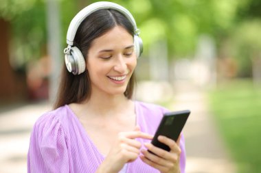 Parkta yürürken cep telefonuyla müzik dinleyen mutlu bir kadın.
