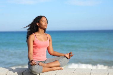 Siyah kadın, güneşli bir yaz gününde plajda yoga egzersizi yapıyor.