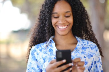 Parkta telefon kullanan mutlu bir siyahi kadının portresi.