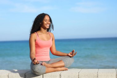 Mutlu siyah yogiler, güneşli bir günde plajda yoga yapıyor.