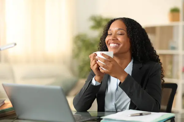 Happy black businesswoman having coffee break breathing and relaxing at home