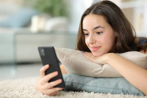 Satisfied woman watching phone content lying on the floor at home