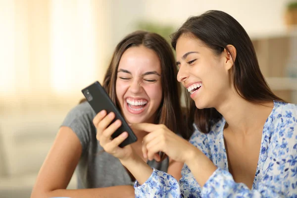Two joyful roommates laughing watching media on phone at home