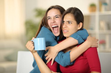 Excited woman hugging to an upset friend at home clipart