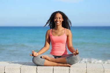 Güneşli bir günde, plajda yoga yapan mutlu zenci bir kadının portresi.