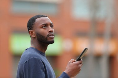 Kaybolan siyah adam sokakta akıllı telefondan yer arıyor.