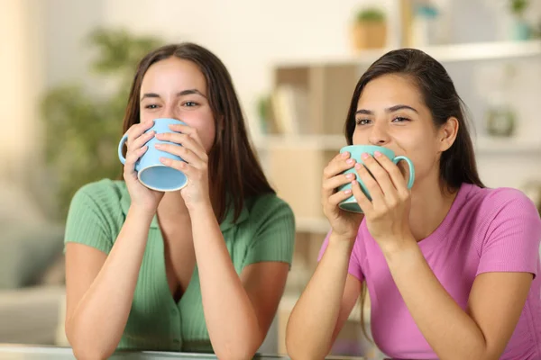 Two funny women drinking coffee at home