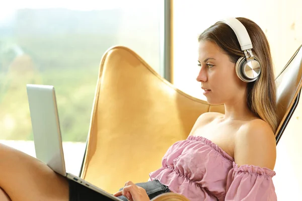 Profile of a woman using laptop and headphone on a chair at home