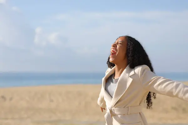 Happy black woman on the beach screaming to the air in winter a sunny day