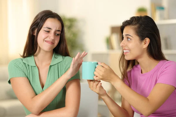 Woman offering coffee cup to a friend who refuses it at home