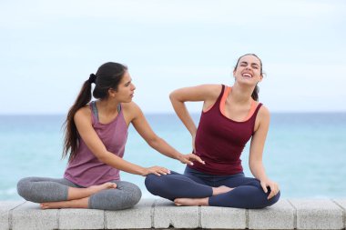 Yogi 'nin sırt ağrısı var. Yoga egzersizi yapıyor ve arkadaşı kumsalda yardım ediyor.