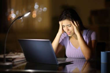 Gece evde dizüstü bilgisayarı olan endişeli bir kadın.
