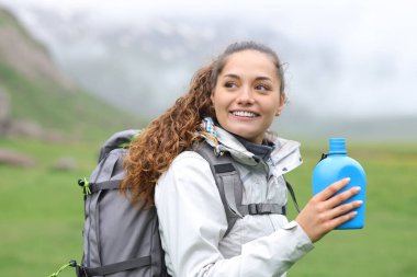 Su kantini tutan mutlu yürüyüşçü doğada yürüyor.