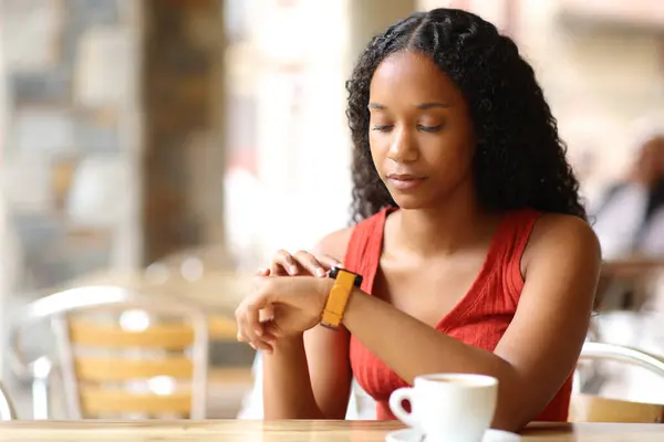 Black serious woman in a restaurant checking smartwatch