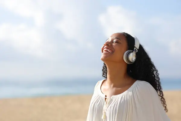 Happy black woman in white breathing fresh air and laughing with headphone listening audio guide