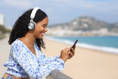 Kulaklık takmış, plajda telefon dinleyen mutlu bir zenci kadının profili.