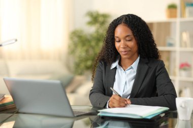 Tele çalışanı evde dizüstü bilgisayarla çalışıyor. Not alıyor.