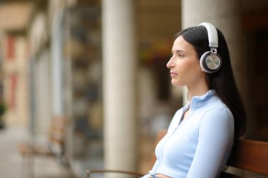 Sokakta kulaklıkla ses dinleyen ciddi bir kadının yan görüntüsü.