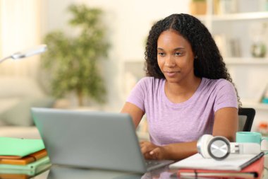 Siyahi bir öğrenci evinde dizüstü bilgisayarla internetten para kazanıyor.