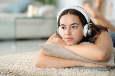 Kulaklıklı düşünceli kadın halıda uzanmış müzik dinliyor.