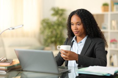 Siyah tele-tele işçisi evde bir dizüstü bilgisayarla içip çalışıyor.