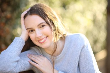 Parkta gülümseyen kameraya bakarak poz veren mutlu dürüst kadın.