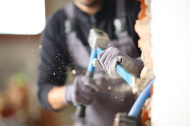 Tadilat altındaki bir evde çekiç ve yamaç kullanarak duvarı yıkan bir inşaat işçisinin portresini yakından çek.