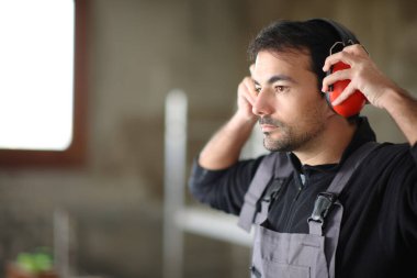 Consruction worker putting noise cancellation headphone in a house under renovation clipart