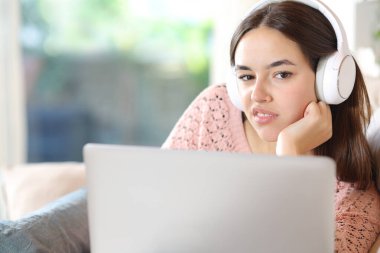 Disgusted woman with headphone and laptop looks at you sitting at home clipart