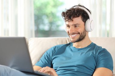 Happy man watching media on laptop sitting on a couch at home clipart